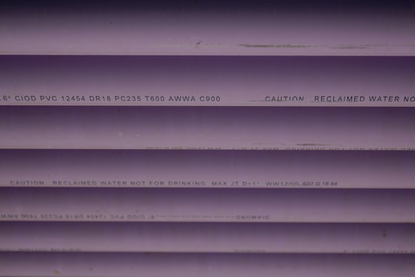 Several purple PVC pipes with black text printed on them. The text includes specifications and a caution that the water is not for drinking.