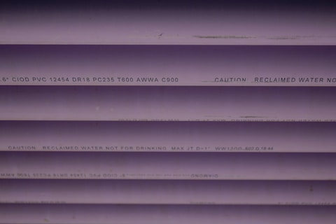 Several purple PVC pipes with black text printed on them. The text includes specifications and a caution that the water is not for drinking.