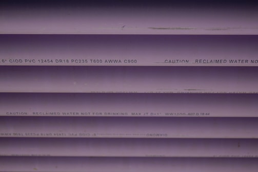 Several purple PVC pipes with black text printed on them. The text includes specifications and a caution that the water is not for drinking.