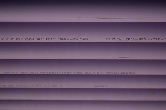 Several purple PVC pipes with black text printed on them. The text includes specifications and a caution that the water is not for drinking.