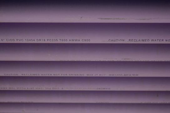 Several purple PVC pipes with black text printed on them. The text includes specifications and a caution that the water is not for drinking.