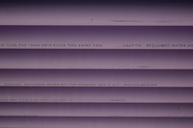 Several purple PVC pipes with black text printed on them. The text includes specifications and a caution that the water is not for drinking.