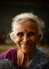 A joyful woman wearing a colorful saree and traditional jewelry, smiling against a soft, warm background.