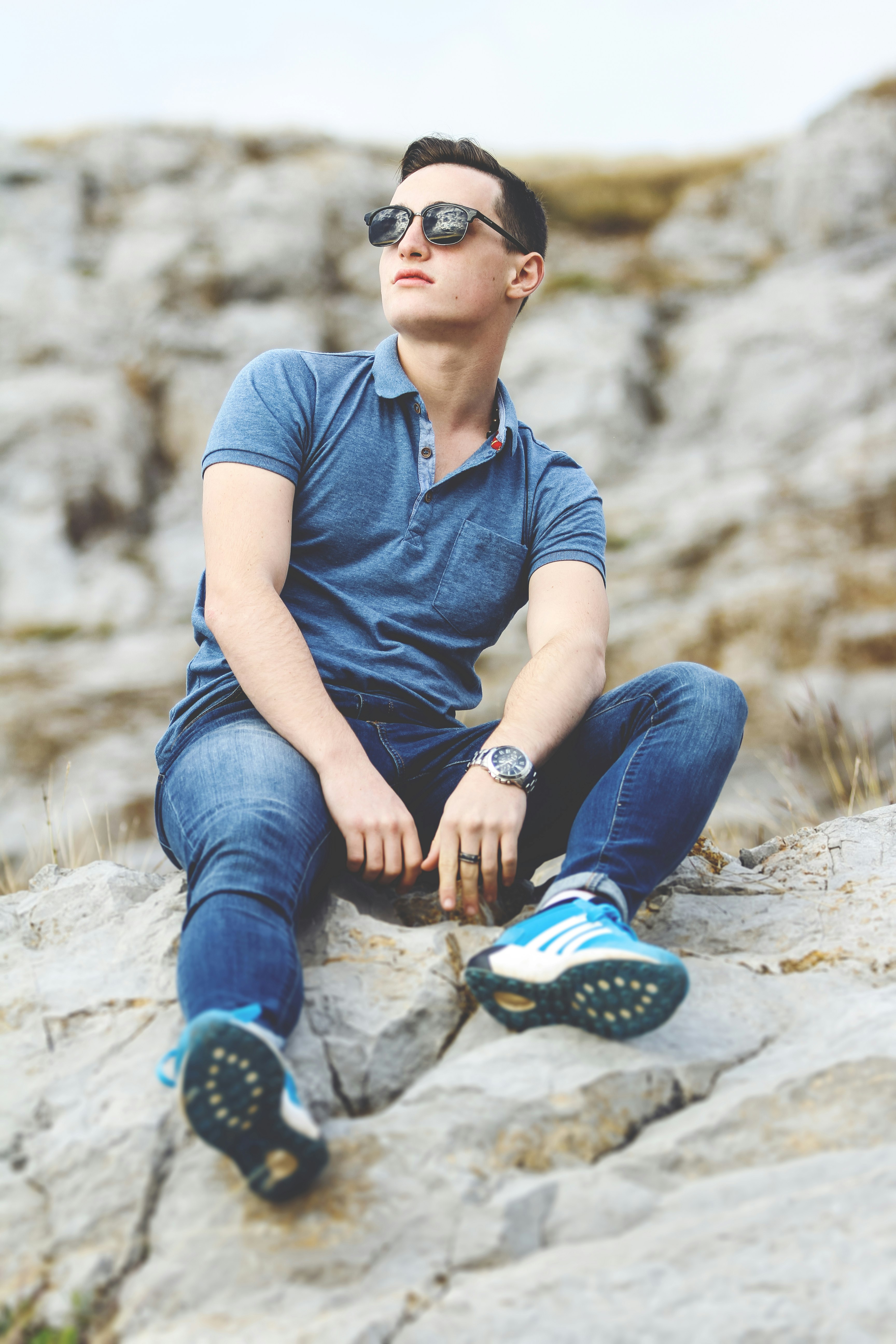 man in blue polo shirt and blue denim jeans sitting on rock during daytime