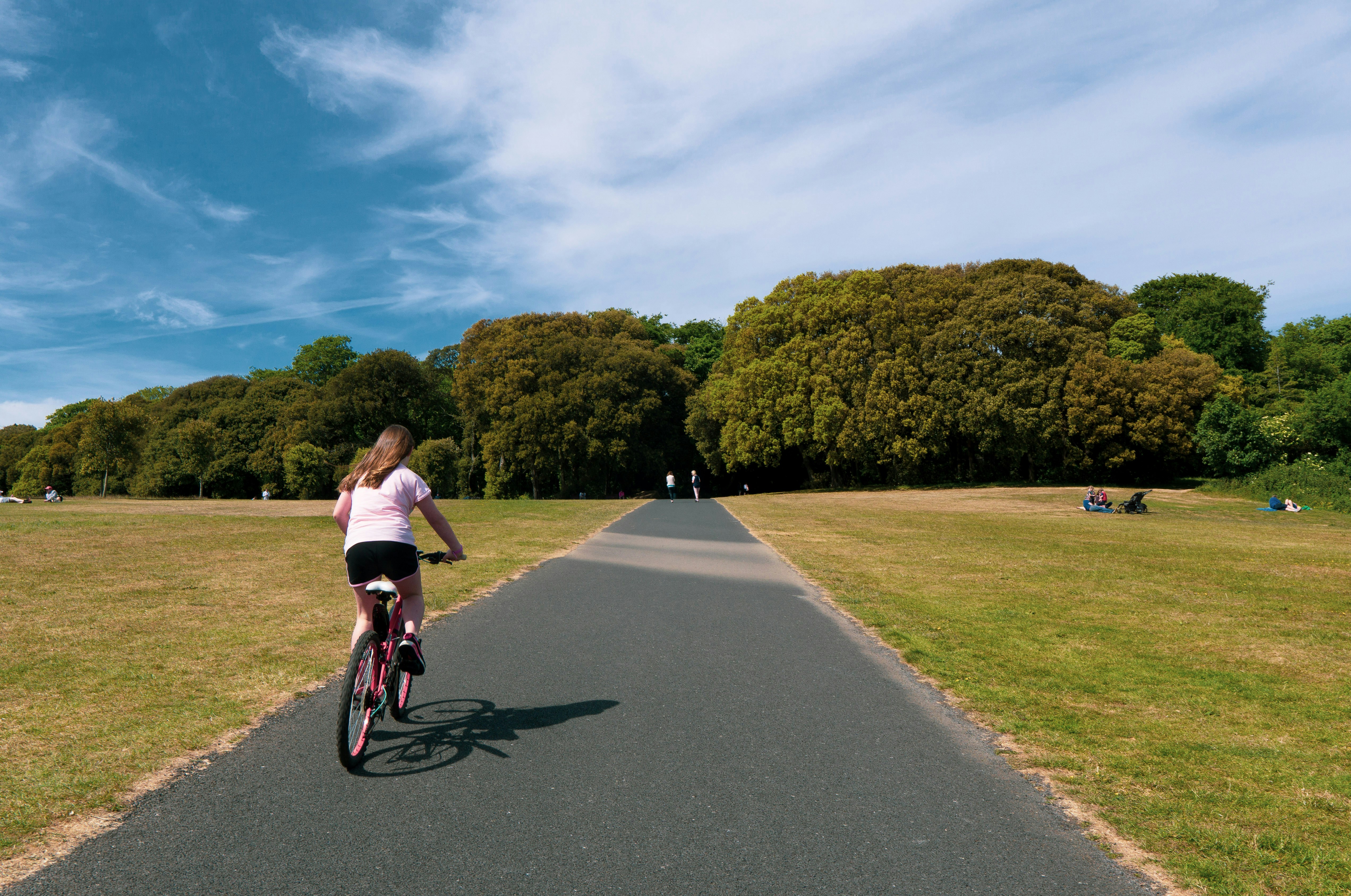 girl in pink shirt riding bicycle on gray concrete road during daytime