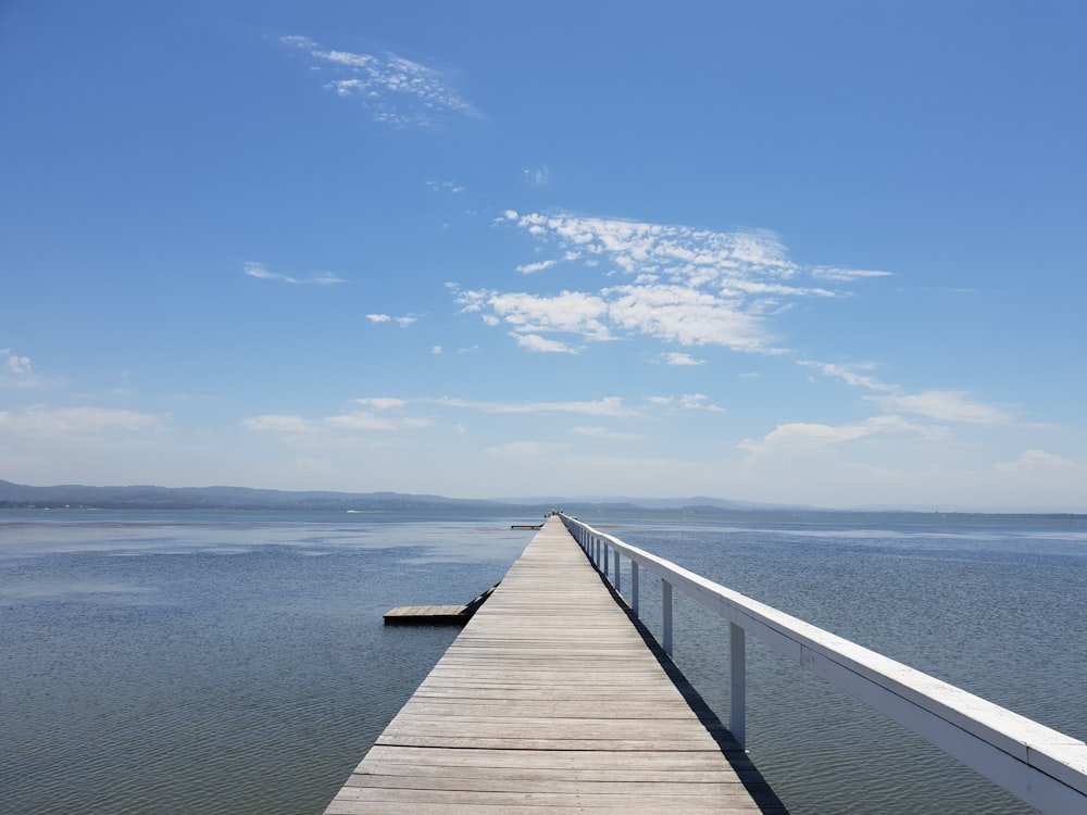 brown wooden dock on blue sea under blue sky and white clouds during daytime