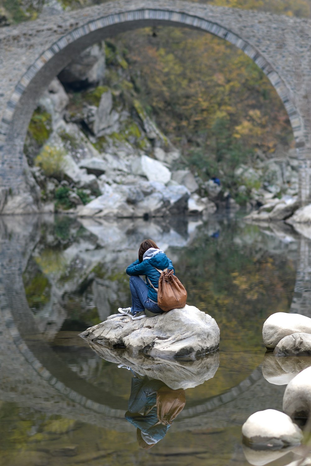 woman in blue jacket sitting on rock