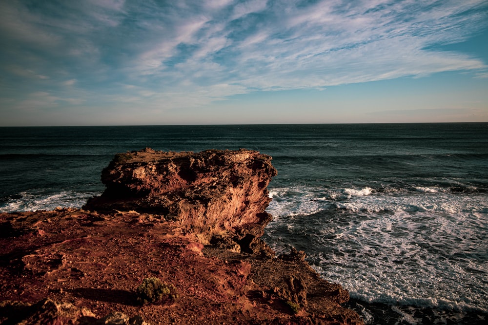 brown rock formation on sea under blue sky during daytime