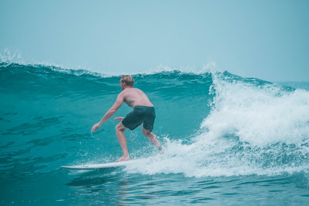 man in blue shorts surfing on sea waves during daytime