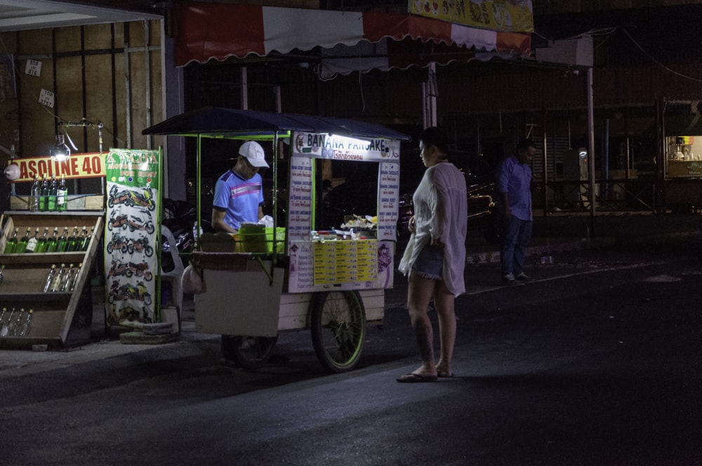man in blue button up shirt and white shorts standing beside food cart