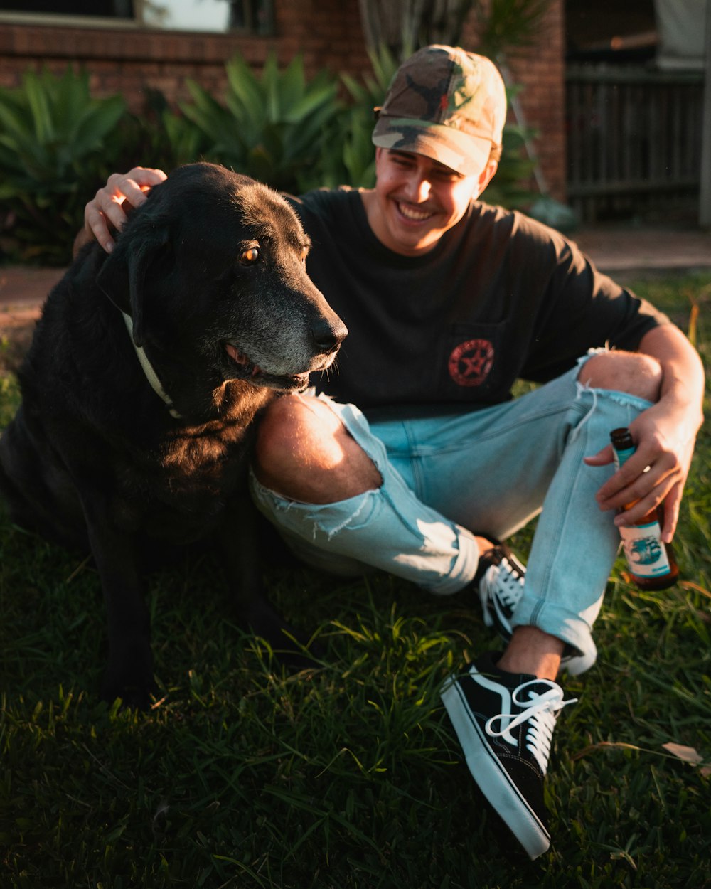 man and woman sitting on grass field beside black labrador retriever