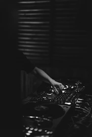 DJ adjusting synthesizer knobs in a dimly lit urban studio filled with vinyl records and music gear.