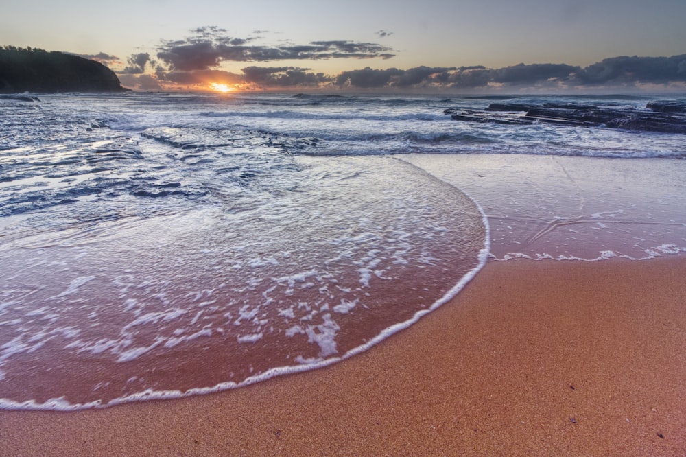 sea waves crashing on shore during sunset