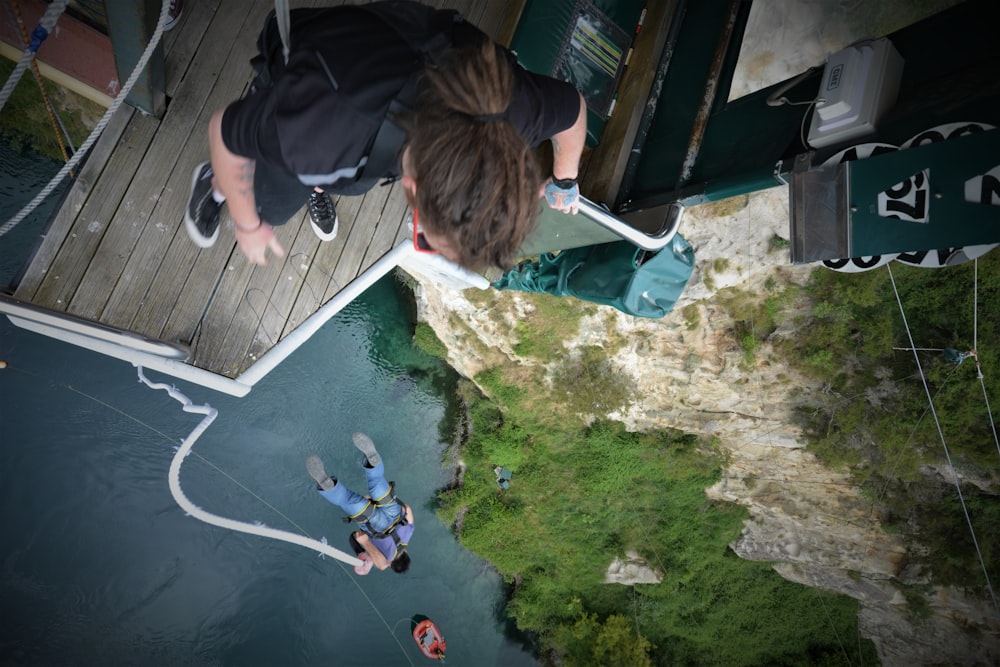 uomo in giacca nera che si siede sulla scala bianca e blu della piscina durante il giorno