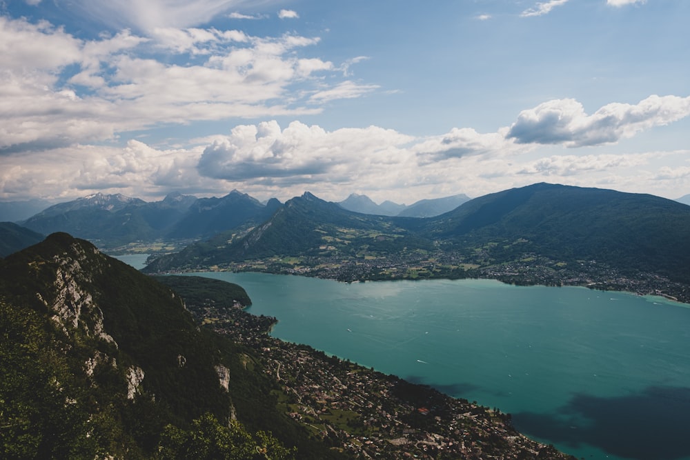 green lake surrounded by mountains under white clouds and blue sky during daytime