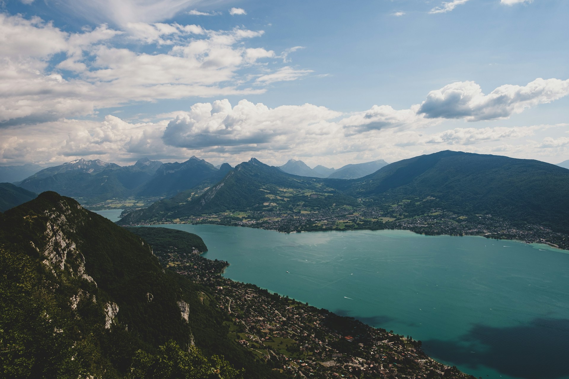 green lake surrounded by mountains under white clouds and blue sky during daytime
