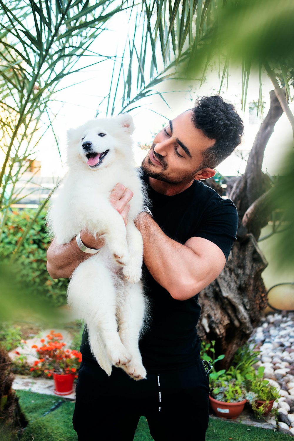 hombre en camiseta negra de cuello redondo sosteniendo un cachorro blanco