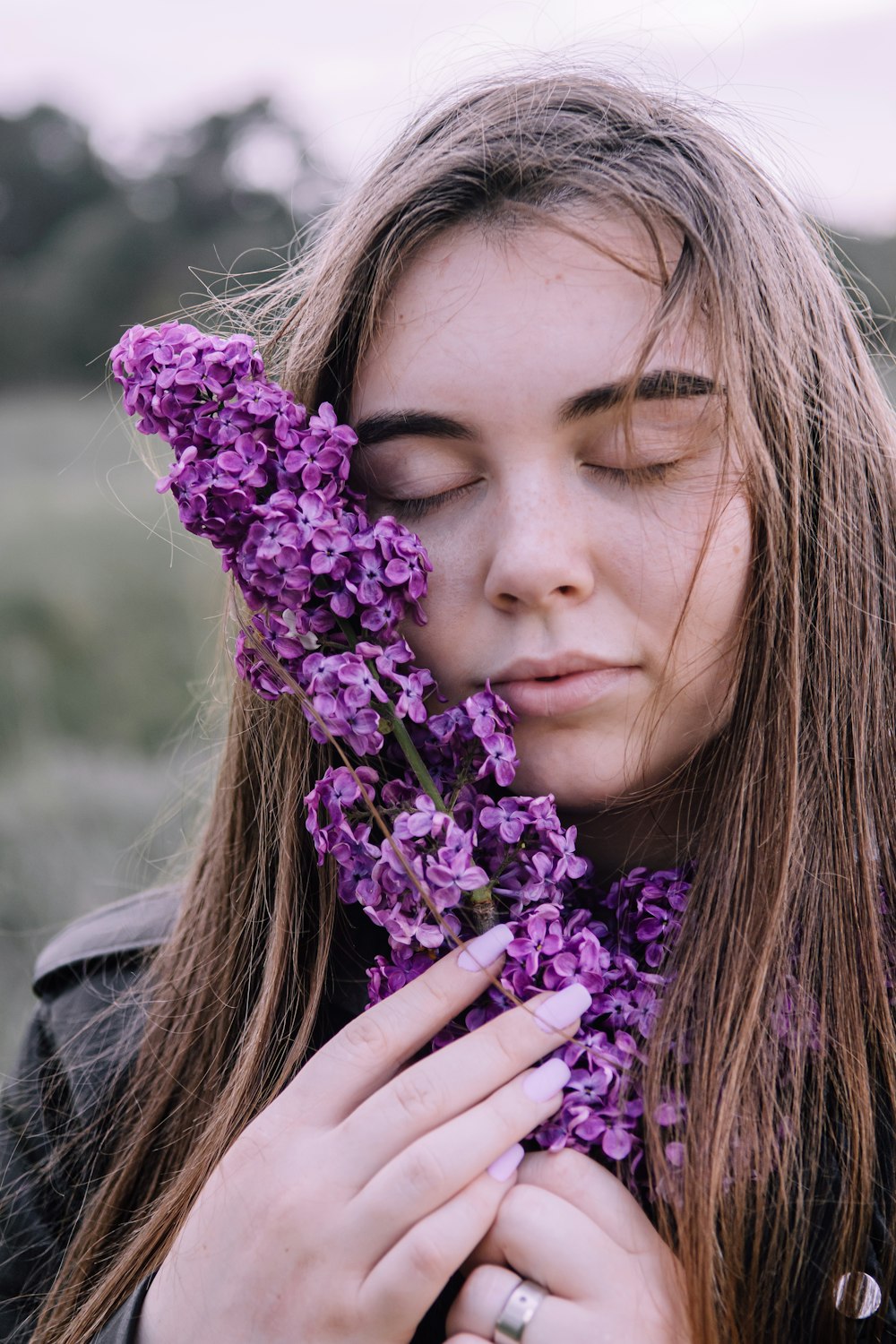 Muchacha en chaqueta gris sosteniendo flores púrpuras