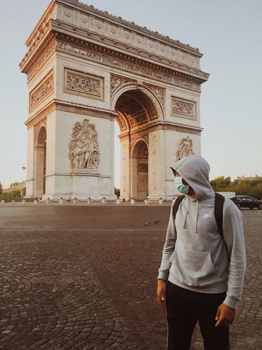 man in gray hoodie standing near brown concrete building during daytime in Arc de Triomphe France