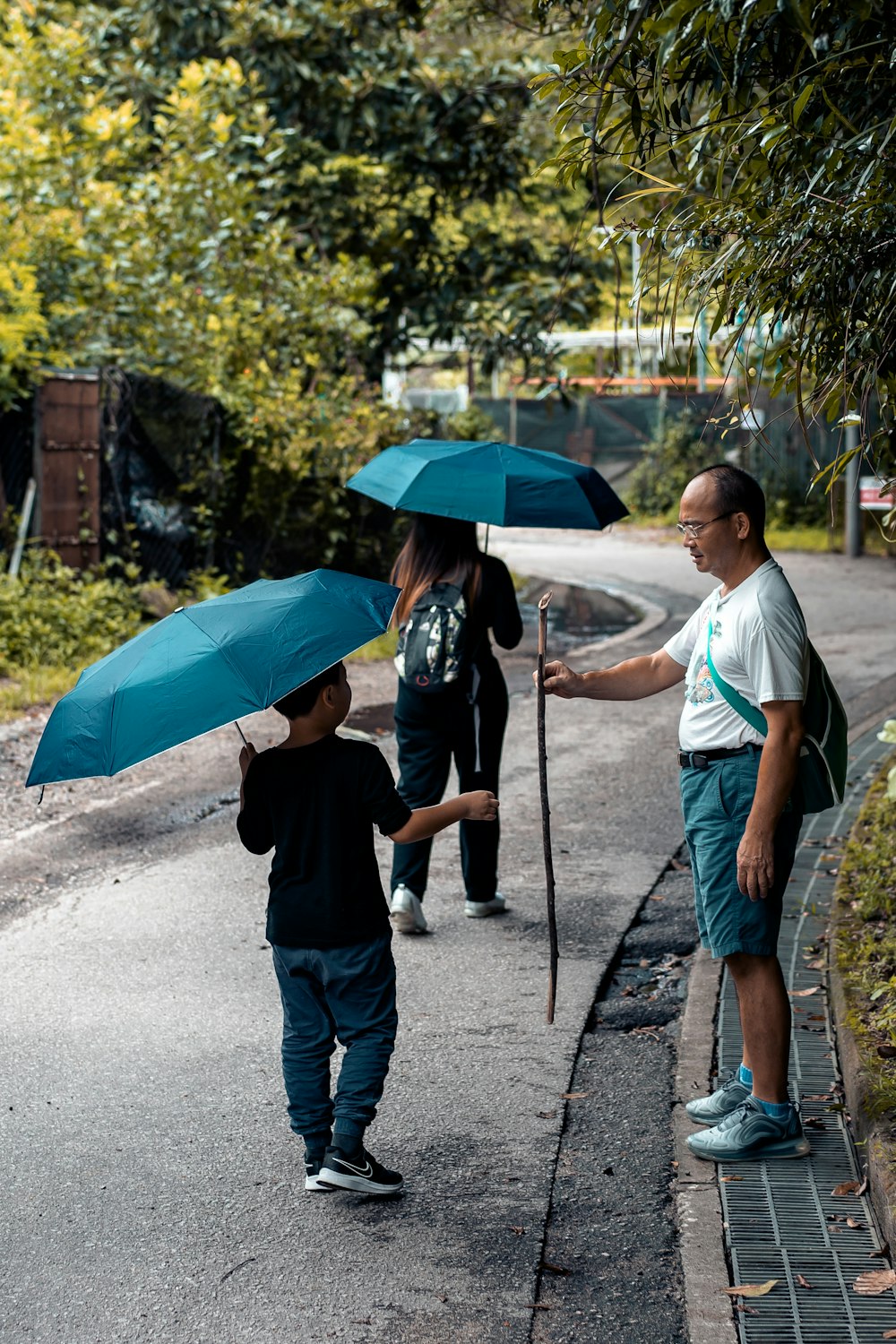 Mann in schwarzem T-Shirt, der tagsüber einen Regenschirm hält und auf der Straße spazieren geht