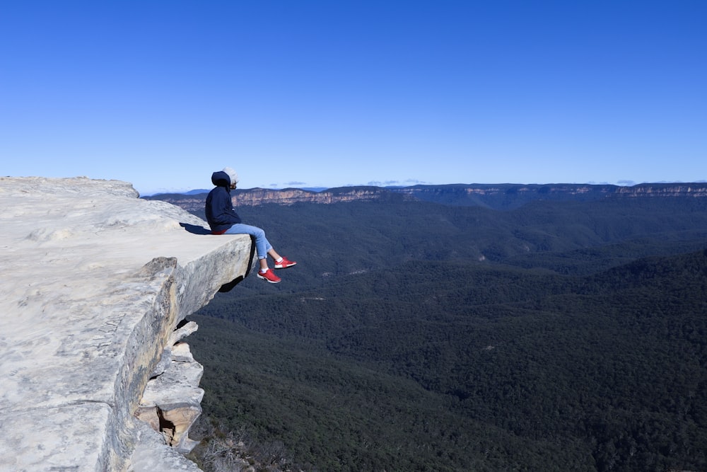 man in black jacket sitting on gray rock during daytime