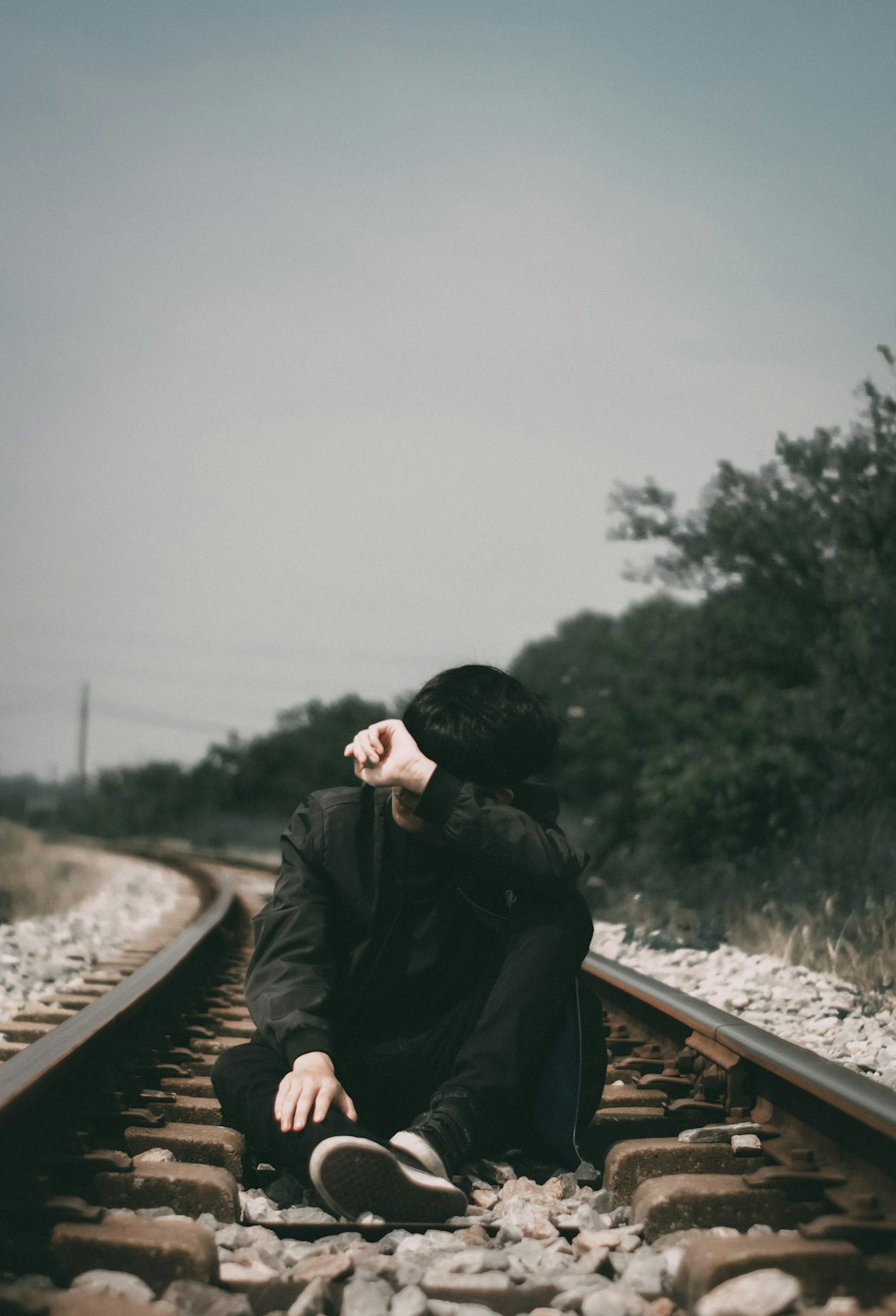 man in black jacket sitting on train rail during daytime