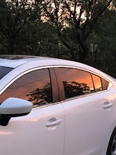 A shiny car parked outdoors with freshly tinted windows reflecting the sunset.