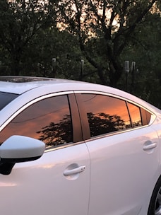 A shiny car parked outdoors with freshly tinted windows reflecting the sunset.