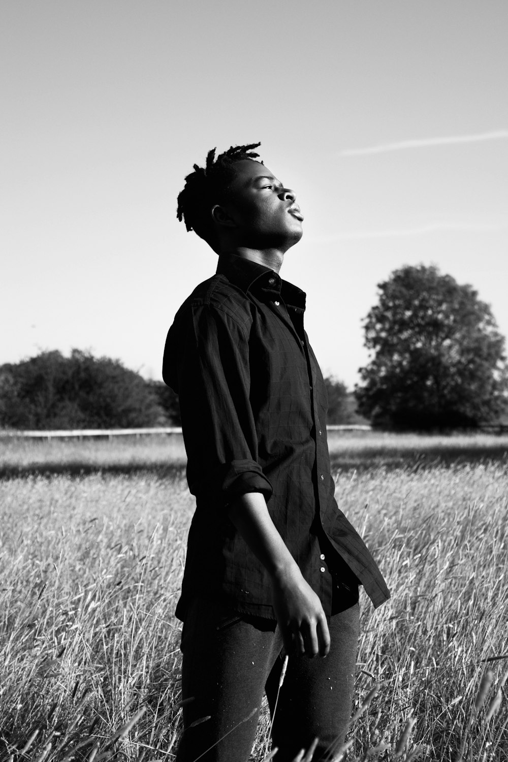 grayscale photo of woman in black jacket standing on grass field