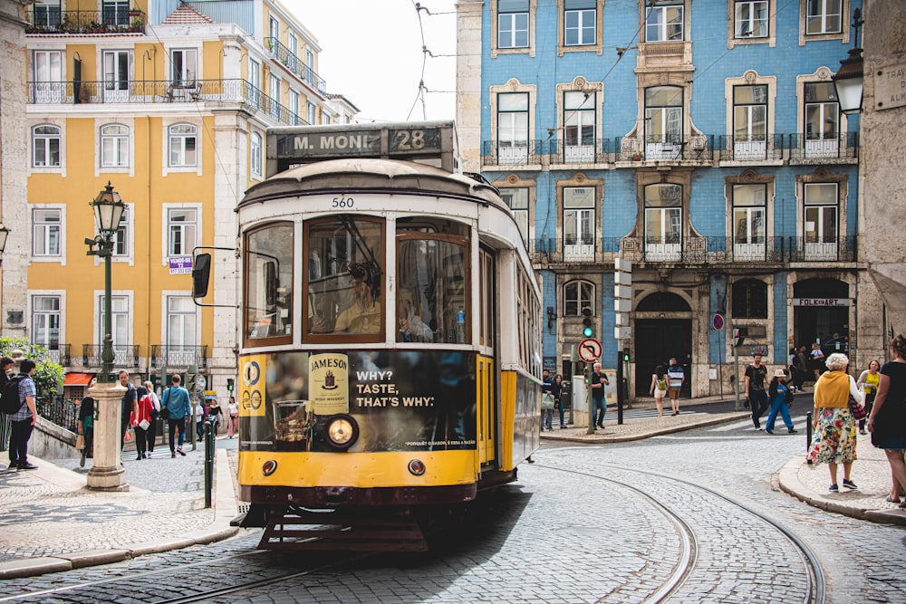 tram giallo e bianco sulla strada vicino all'edificio in cemento bianco durante il giorno