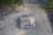 A stencil-style artwork is painted on a concrete surface, featuring a person's face and the text 'I'm kind of a big deal'. Surrounding the artwork, there are patches of grass, small rocks, and more concrete.
