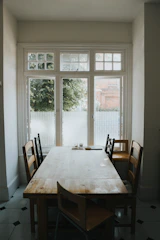 A sleek walnut dining table with matching chairs, bathed in natural light on a brown-toned floor.