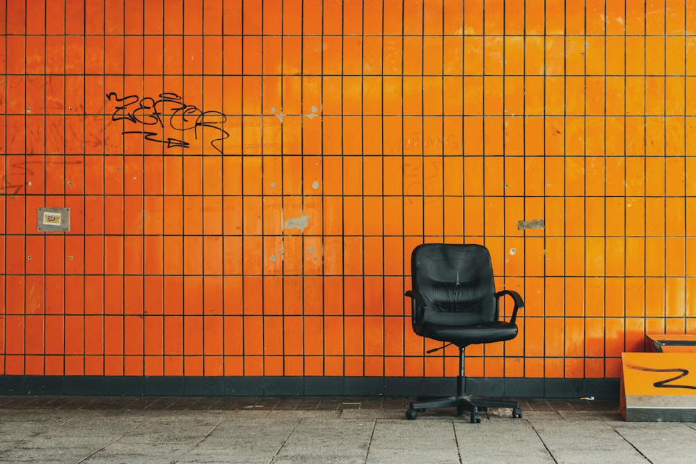 Chaise roulante en cuir noir à côté d’un mur orange