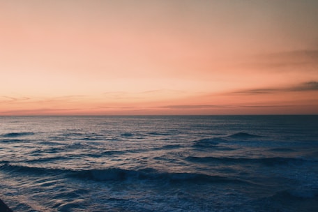 A serene ocean at sunset with warm orange and pink hues reflecting on gentle waves.