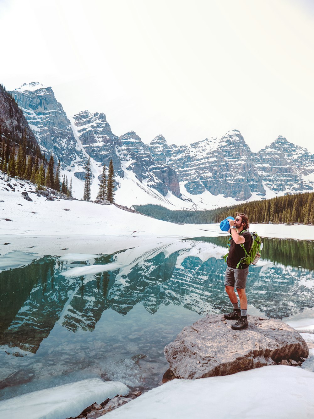 man in black t-shirt and black shorts standing on rock near snow covered mountain during