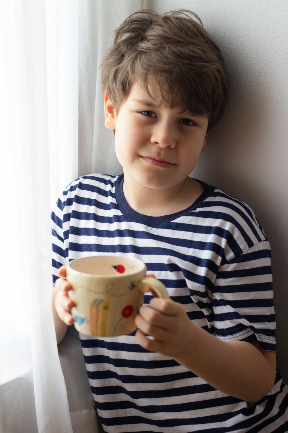 boy in blue and white striped crew neck shirt holding white ceramic mug