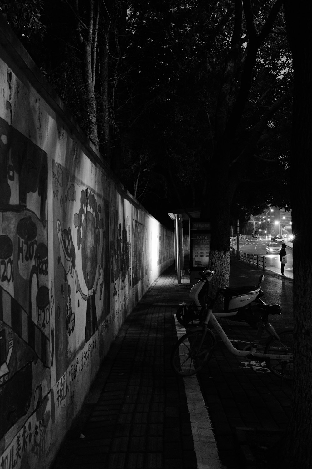 grayscale photo of man sitting on bench beside wall with graffiti