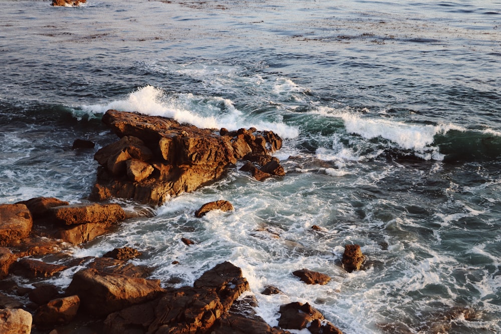 formação rochosa marrom no mar durante o dia