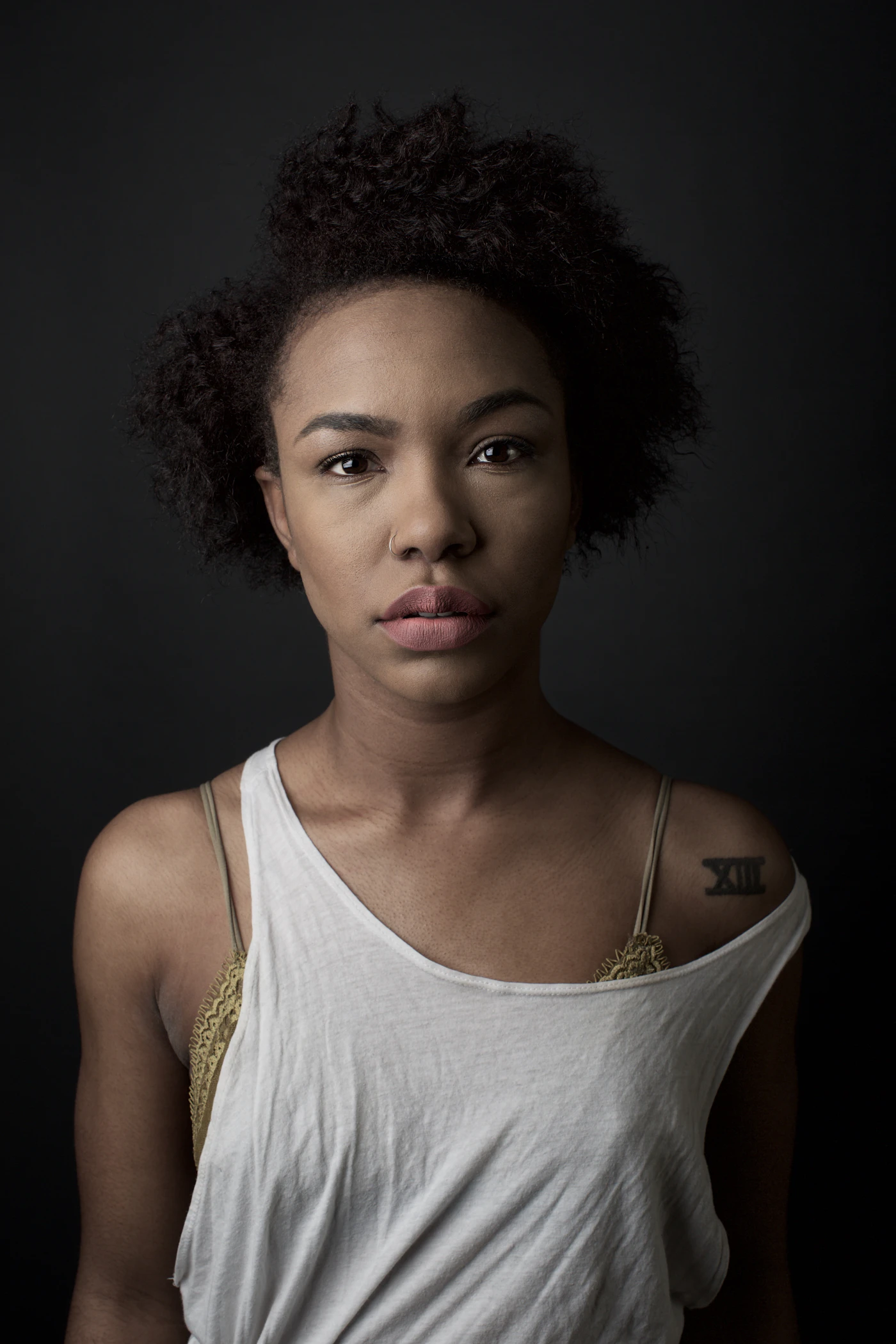 Portrait of a woman with a short, sculpted coily crop, lit from one side against a dark backdrop