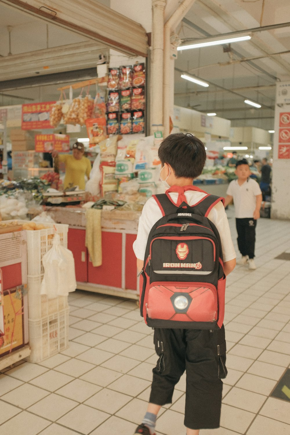 boy in black white and red backpack standing in front of food display counter