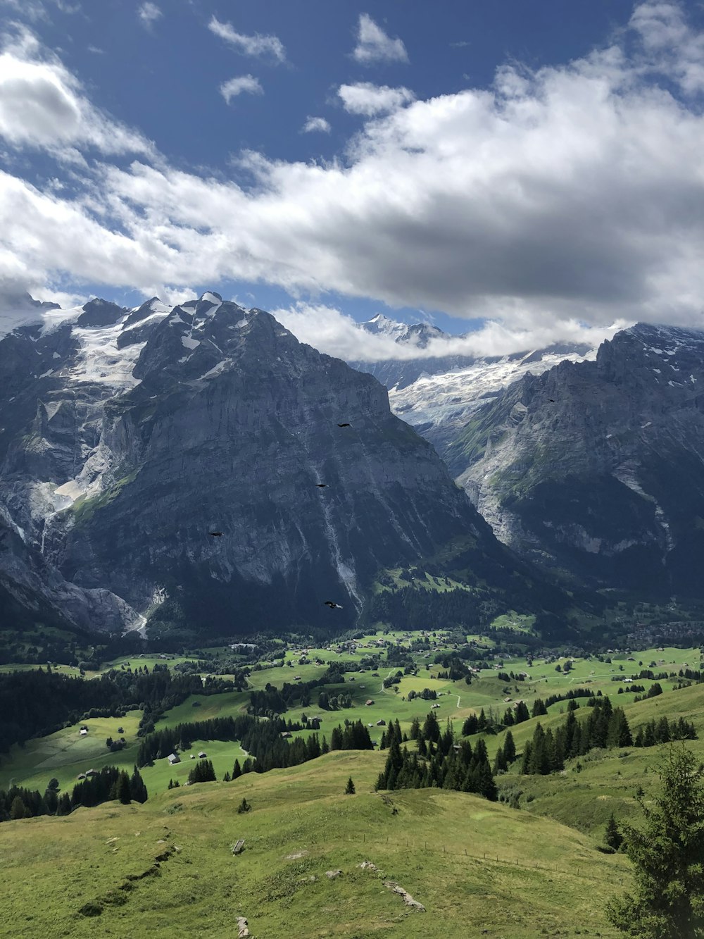 green grass field near mountain under white clouds and blue sky during daytime