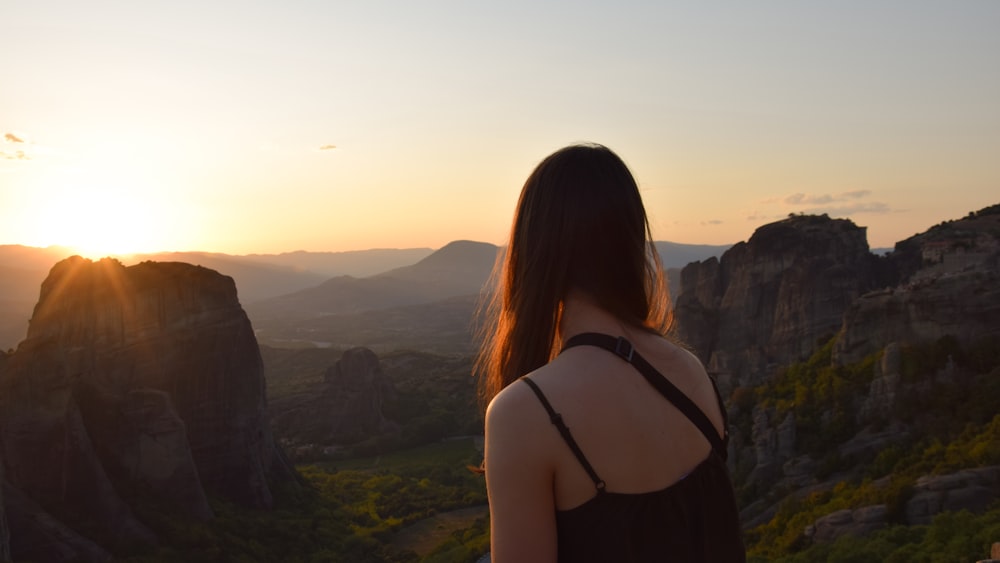 woman in black tank top standing on rock formation during sunset
