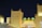 A Moroccan-themed building is illuminated at night with bright yellow lighting on traditional architecture featuring crenelated walls and towers. A prominent sign displaying the word 'MOROCCO' in bold yellow letters is visible.