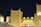 A Moroccan-themed building is illuminated at night with bright yellow lighting on traditional architecture featuring crenelated walls and towers. A prominent sign displaying the word 'MOROCCO' in bold yellow letters is visible.