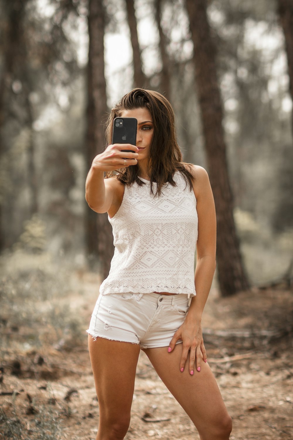 woman in white tank top holding black smartphone
