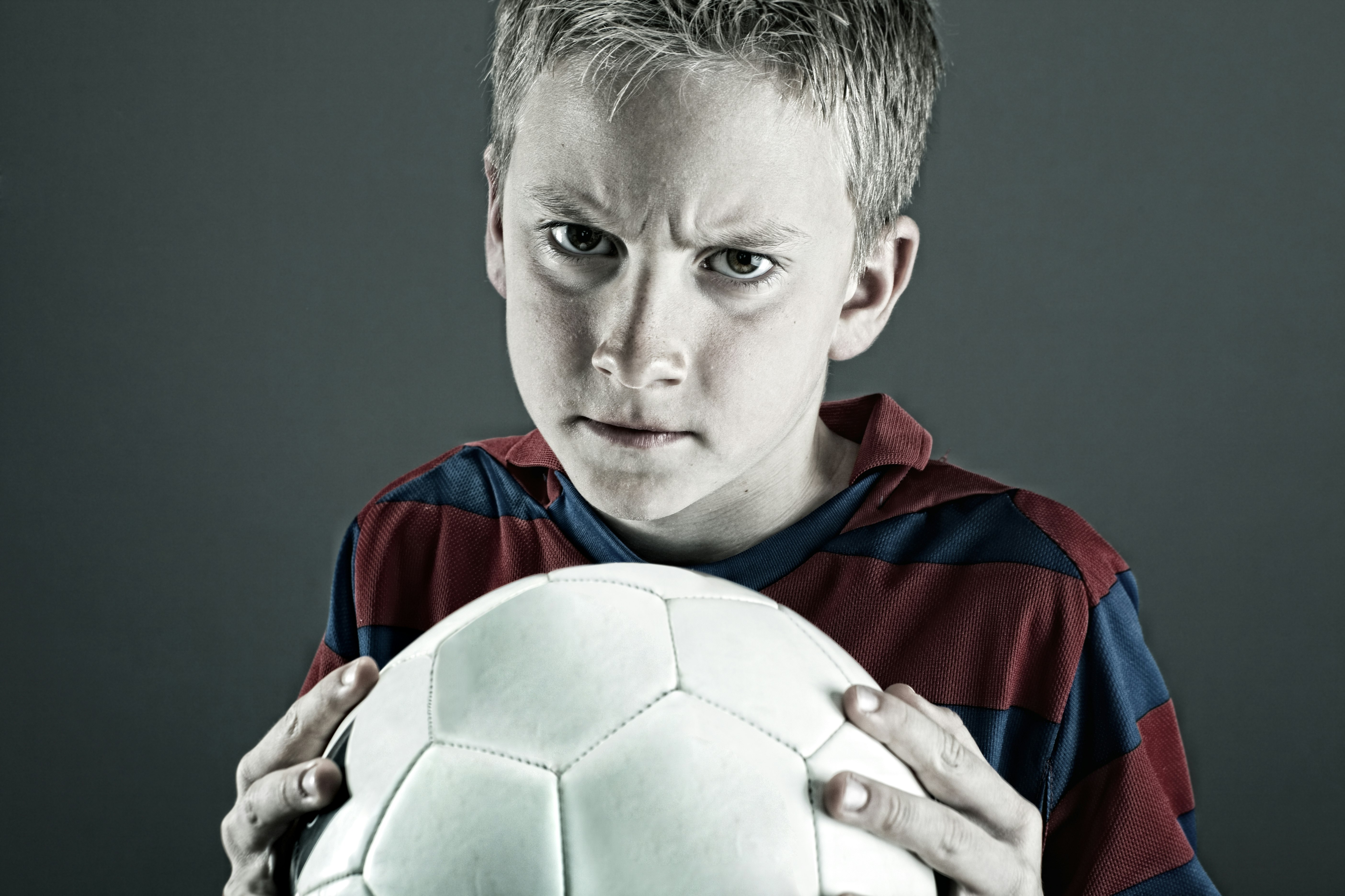 boy in blue and red jersey shirt holding white soccer ball