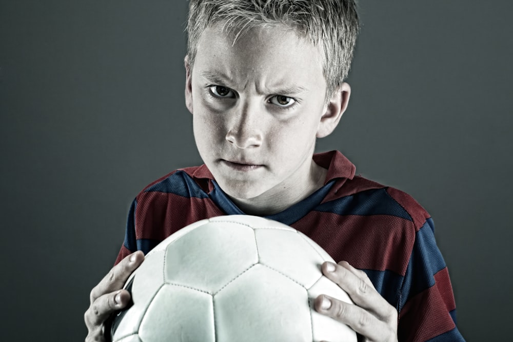 boy in blue and red jersey shirt holding white soccer ball