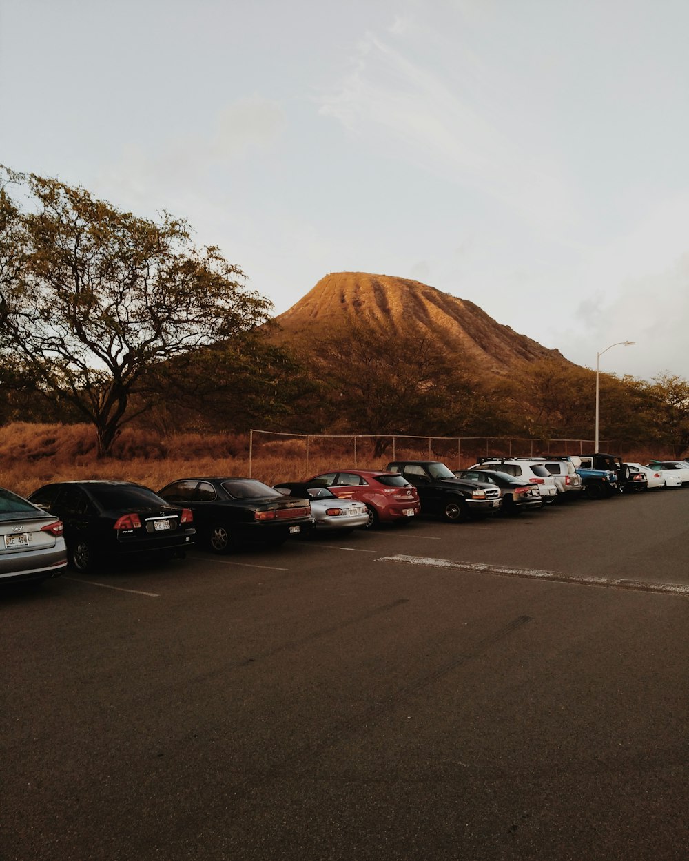 cars parked on parking lot near brown mountain under white clouds during daytime