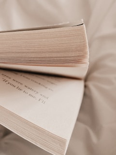 Close-up of an open book resting on a wooden desk with soft natural light highlighting the textured pages.