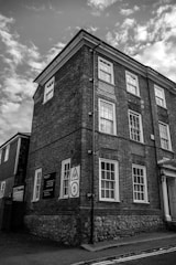 A tall brick building with multiple windows appears to be a historical or older structure. It has a street sign indicating a school zone with a speed limit. The sky is partly cloudy, creating a dramatic atmosphere in the black-and-white imagery.